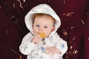 fall photo of baby laying on a blanket, holding a leaf