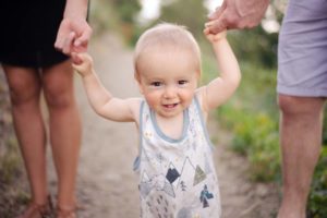 baby taking his first steps while mom and dad are holding his hands